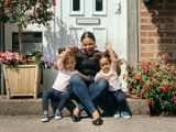 Lady with her 2 children smiling sitting at their front door in the sunshine 