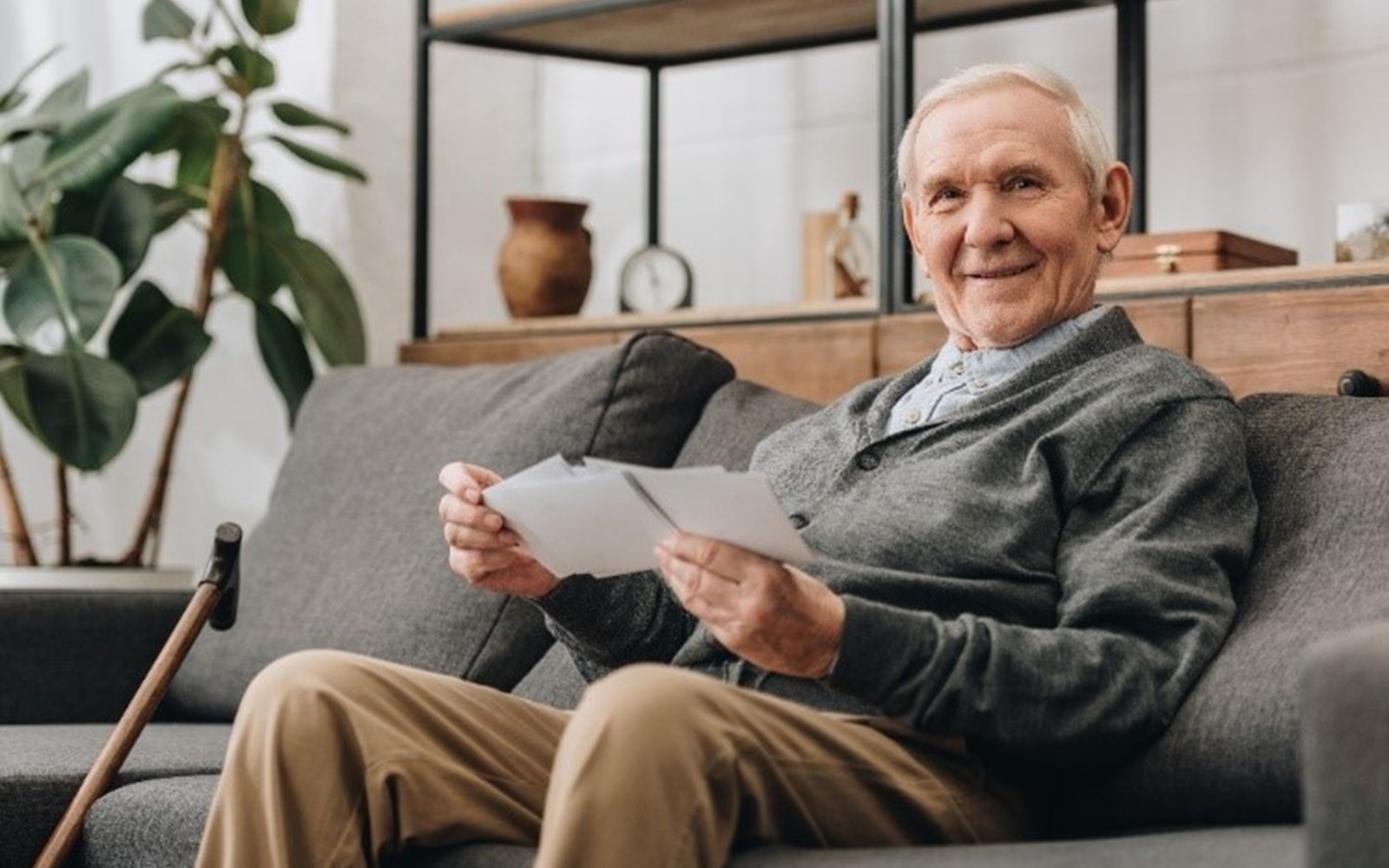 John, smiling from his sofa holding some cards in his hands