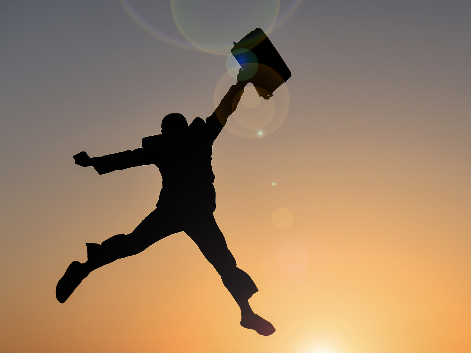Shadow figure in sunset jumping into the air with a briefcase 