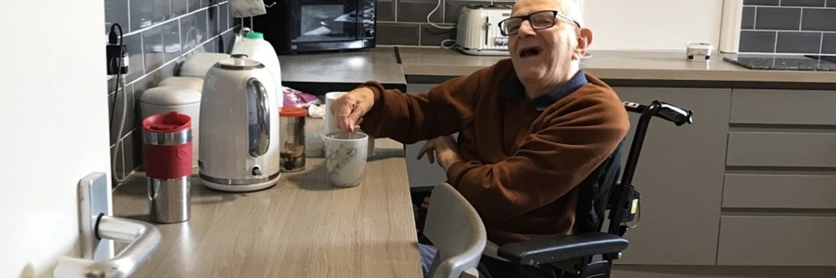 tenant James making a brew at his kitchen counter in his wheelchair, smiling 