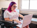 Lady with bright coloured pink and purple hair smiling on laptop 